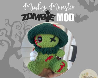 May include: Green crocheted zombie monster plush toy with red accents and a green hat. The toy has one eye and a stitched X over its mouth. The toy is holding a white crocheted object in its hand. The text "Mushy Monster ZOMBIE MOD" is written above the toy.