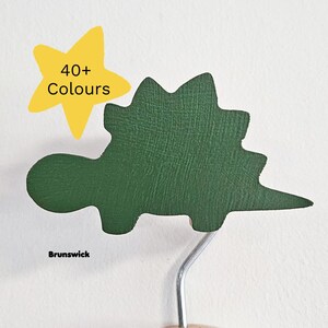 May include: A green dinosaur-shaped object with a textured surface. A yellow star-shaped graphic with the text "40+ Colours" is in the upper left. The word "Brunswick" is at the bottom.