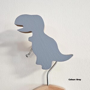 May include: A grey dinosaur-shaped wall hook. The wooden hook is painted grey and has a silver metal hook extending from its belly. The base is made of natural wood. The text "Colour: Grey" is in the bottom right corner.