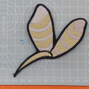 Puede incluir: Un parche de hierro en forma de mariposa con un patrón a rayas en beige y marrón.