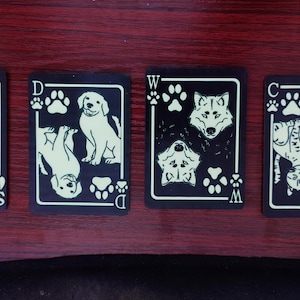 May include: Four black playing cards with white illustrations of animals. The cards feature a ram, two dogs, a wolf, and two cats. Each card has a white border and suit symbols.