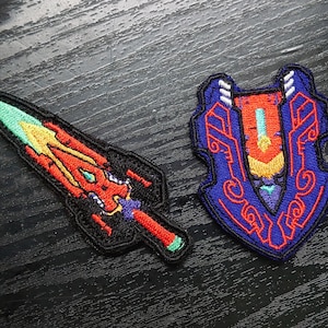 May include: Two embroidered patches, one depicting a red and yellow sword with a blue and green blade, and the other a blue and red shield with intricate designs.