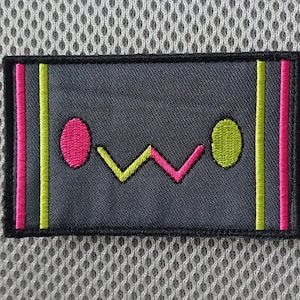 May include: A gray embroidered patch with a pink and green design. The design features two circles, one pink and one green, and a stylized "W" shape in between.