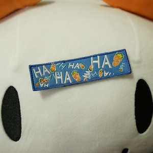 May include: A blue fabric patch with white embroidery that says "HA HA HA" with small carrot images scattered around the text.