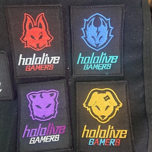 May include: Four black fabric patches with embroidered images of foxes in different colours. Each patch has the text "hololive GAMERS" in white.