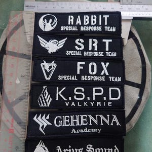 May include: A set of six black embroidered patches with white lettering and logos. The patches feature the names "RABBIT SPECIAL RESPONSE TEAM", "SRT SPECIAL RESPONSE TEAM", "FOX SPECIAL RESPONSE TEAM", "K.S.P.D VALKYRIE", "GEHENNA Academy", and "Arius Squad".
