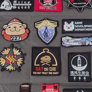 Puede incluir: Una colección de parches bordados con varios diseños, incluyendo una calavera y huesos cruzados con el texto "Eat or Die", un oso con un sombrero rojo con el número "227", una estrella con una doble "S" en el centro, una nave espacial con el número "70" y un edificio con el texto "General Student Council".
