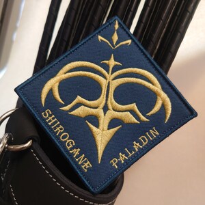 May include: A blue and gold embroidered patch with the words "Shirogane Paladin" and a stylized design.