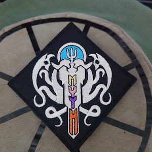 Peut inclure: Patch noir en forme de diamant avec un motif brodé blanc représentant une créature avec des tentacules et un trident. La créature a un corps blanc avec une bande verticale arc-en-ciel au centre.