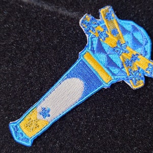 May include: An embroidered patch shaped like a microphone, featuring blue and yellow colours with a star design.
