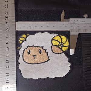 May include: Embroidered patch featuring a cartoon ram with white wool, a tan face, and yellow horns. The patch is approximately 3 inches wide. The patch is on a black background.