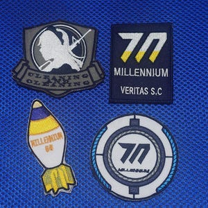 May include: Four embroidered patches with various designs. One patch features a shield with a silhouette and the words "CLEANING CLEANING". Another has the number "70" and the words "MILLENNIUM VERITAS S.C". A third patch is shaped like a bomb with the words "MILLENNIUM 60". The last patch is circular with the number "70".