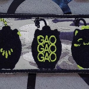 May include: Embroidered patch with a black border featuring three stylized black shapes with neon green accents. The patch includes the text "LA LION" and a Leo zodiac symbol. The background has a cloud-like pattern.