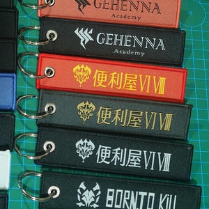 以下が含まれることがあります： 赤、黒、オレンジなど、さまざまな色の刺繍キーホルダーのコレクション。各キーホルダーには、「GEHENNA Academy」や「BORN TO KILL」などのユニークなテキストとデザインがあり、シルバーのキーリングに取り付けられています。