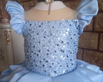 Könnte beinhalten: Ein hellblaues Tüll- und Satin-Kleid mit einem Pailletten-Oberteil und Puffärmeln. Das Kleid hat eine schwarze Halskette mit einem silbernen Anhänger.