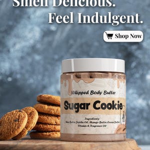 May include: A jar of "Sugar Cookie" whipped body butter with a white lid, next to a stack of chocolate chip cookies. The jar's label lists ingredients and the text "Smell Delicious. Feel Indulgent. Shop Now."