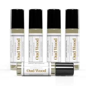 May include: Five glass bottles of Oud Wood fragrance oil. Each bottle has a black cap and a white label with the text "Jersey Botanical Luxury Line Our Impression of Oud Wood Highly Concentrated. For External Use Only."
