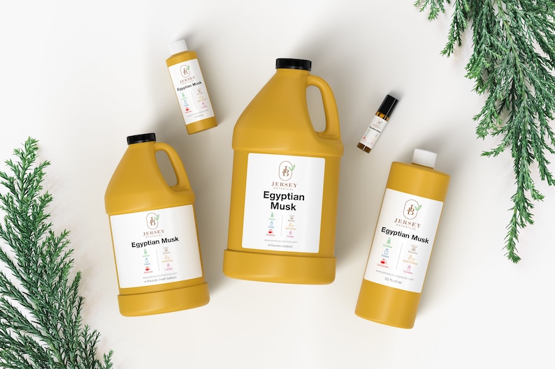 May include: Four bottles of Egyptian Musk essential oil in different sizes. The bottles are yellow and have a white label with the text "Jersey Botanicals Egyptian Musk" on them. The bottles are arranged on a white surface with green foliage in the background.