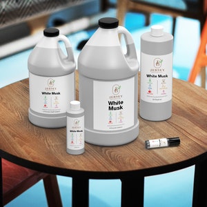 May include: Four bottles of White Musk fragrance oil in various sizes, from a small sample bottle to a large gallon jug. The bottles are on a wooden table with a black metal base.