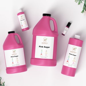 May include: Four pink bottles of Jersey Botanicals Pink Sugar fragrance oil in different sizes. The bottles are on a white surface with green foliage in the background.