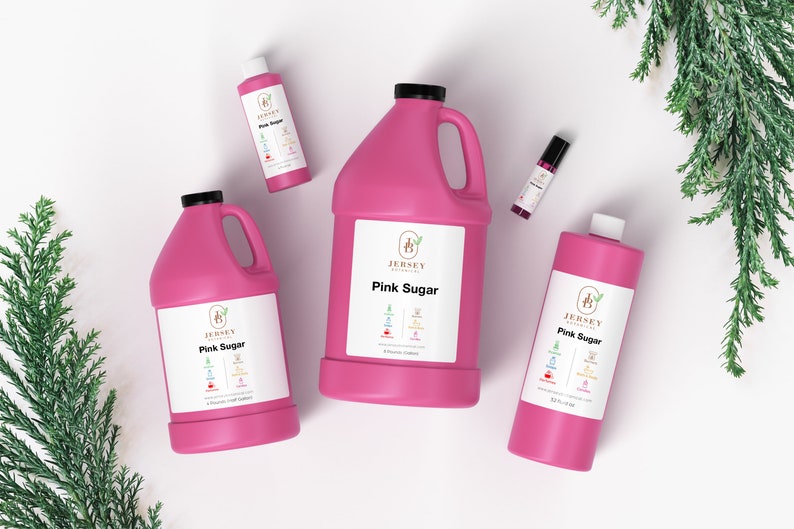 May include: Four pink bottles of Jersey Botanicals Pink Sugar fragrance oil in different sizes. The bottles are on a white surface with green foliage in the background.