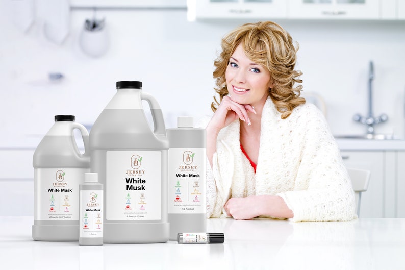 May include: Four bottles of White Musk essential oil in various sizes, from a small roller bottle to a large 32 oz bottle. The bottles are all white with a black label and the Jersey Botanicals logo. The bottles are sitting on a white table in front of a woman wearing a white sweater.