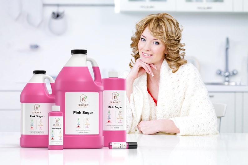 May include: Four bottles of pink sugar scented liquid in various sizes, with the Jersey Botanicals logo and product name on the labels. The bottles are arranged on a white surface with a woman in the background.