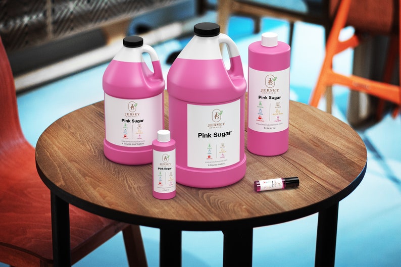 May include: Four bottles of pink sugar-scented liquid in various sizes, from a small 1 oz bottle to a large 1 gallon jug, all with the same label featuring the text "Jersey Aromatics" and "Pink Sugar". The bottles are on a wooden table.