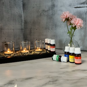 May include: A set of six essential oil bottles with labels for rose, lemongrass, lemon, strawberry, and grass. The bottles are arranged on a wooden tray with three lit tea lights.