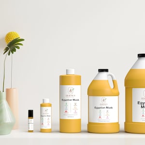 May include: Four bottles of Egyptian Musk essential oil in different sizes. The bottles are yellow and have a white label with the text "Jersey Botanicals Egyptian Musk" on them. The bottles are arranged in a row from smallest to largest.