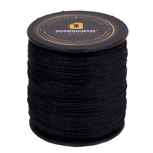 May include: A large spool of black cord wrapped tightly around a black plastic cylinder. The top label is black with gold text reading DAMODARAM ENTERPRISE, SINCE 2013, 100% PREMIUM & EXPORT QUALITY, MADE IN INDIA, and MADE WITH LOVE FOR YOU.