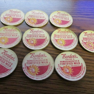 May include: Ten round, vintage Borden's Grade A Homogenized Vit D Fortified Milk cardboard bottle caps. Each cap features a red and cream color scheme with a yellow sunflower graphic and the Borden's brand name printed in red script text.
