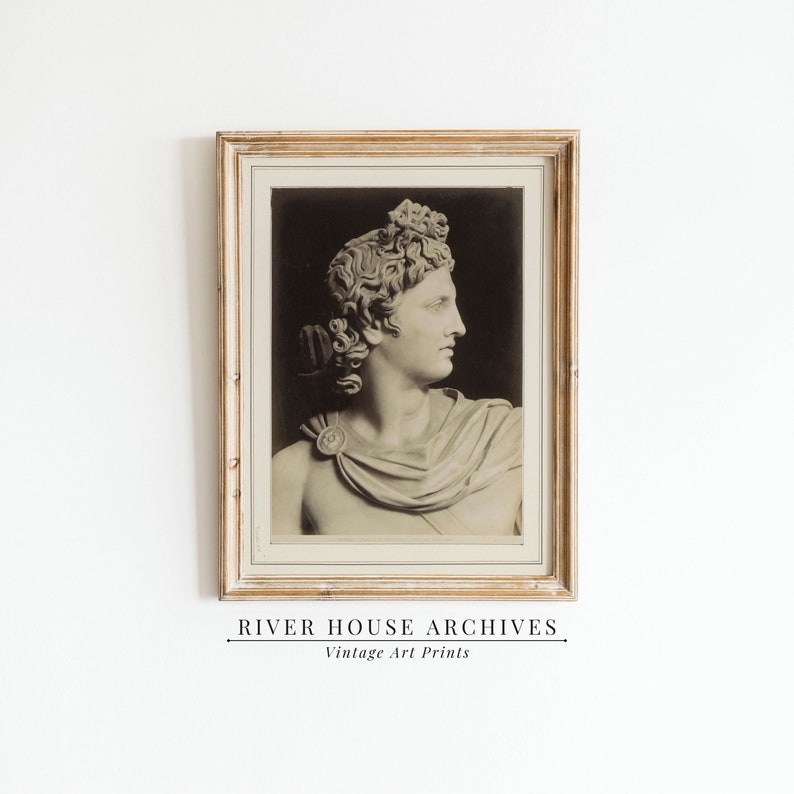 May include: A vintage black and white photograph of a marble bust of a man with a laurel wreath on his head. The bust is framed in a gold frame.