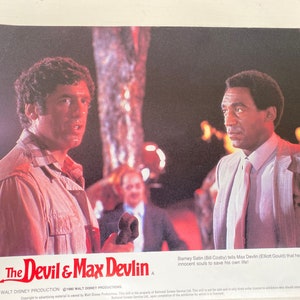 Op de afbeelding: Een filmposter voor de film "The Devil & Max Devlin" met Bill Cosby en Elliott Gould. De poster heeft een rode achtergrond met de titel in witte letters. De acteurs zijn casual gekleed en staan voor een wazige achtergrond.