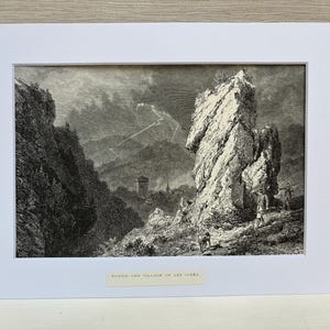 May include: Black and white landscape print of a rocky mountain scene with a tower and village in the distance. The print is matted in white and labeled "TOWER AND VILLAGE OF LES CLERES".