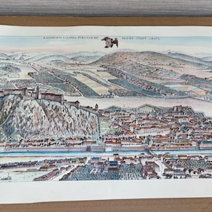 Könnte beinhalten: Eine detaillierte, alte Karte von Graz, Österreich, mit einer Vogelperspektive der Stadt und ihrer Umgebung. Die Karte ist reich an Farben wie Blau, Grün, Braun und Rot, die die Architektur, den Fluss und die Berge hervorheben. Der Text oben lautet "KAISERLICH U. LANDS. FURSTLICH."