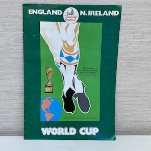 May include: A green and white program for a soccer match between England and Northern Ireland. The program features a stylized illustration of a soccer player's leg kicking a ball. The text "ENGLAND N.IRELAND" is printed in large, bold letters at the top of the program. The text "WORLD CUP" is printed in large, bold letters at the bottom of the program.