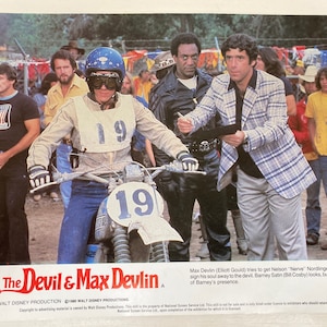 Puede incluir: Un póster de película para la película "The Devil & Max Devlin" que presenta una escena con un joven en una moto de cross, un hombre con una camisa a cuadros y un hombre con una chaqueta de cuero. El póster incluye el texto "A Walt Disney Production" y "1980 Walt Disney Productions".
