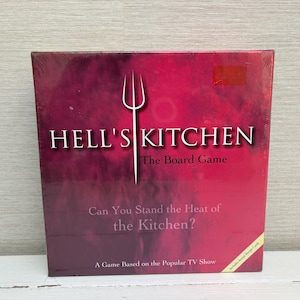 Könnte beinhalten: Ein Brettspielkarton für "Hell's Kitchen" mit einem roten Farbverlauf im Hintergrund. Der Spieletitel und ein weißes Gabel-Logo sind zentriert. Der Text lautet "Can You Stand the Heat of the Kitchen?" und "A Game Based on the Popular TV Show."