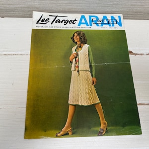 May include: A vintage knitting pattern booklet featuring a woman wearing a white Aran knit dress and vest. The cover features the text "Lee Target Aran 8921 1/16" and "Motoravia and other double knitting qualities".
