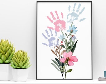Puede incluir: Una impresión enmarcada con un diseño de acuarela de un ramo de flores con tres huellas de manos en rosa, azul y morado. Las huellas de manos están dispuestas en forma de triángulo sobre las flores.