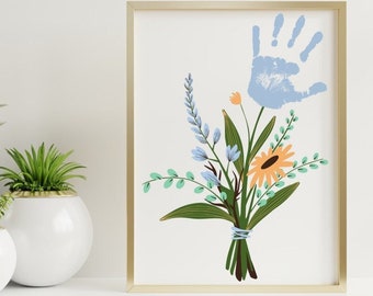 Puede incluir: Una impresión enmarcada en dorado con una huella de mano azul y un ramo de flores en tonos azules, verdes y naranjas. Las flores están dispuestas en un jarrón.