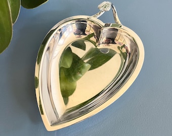 May include: A polished silver leaf-shaped dish with a stem handle. The dish has a smooth, reflective surface and a shallow bowl. The design is elegant and decorative, suitable for serving small items or as a decorative accent.