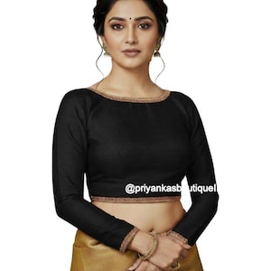May include: Black long-sleeve blouse with gold trim around the neckline and cuffs. The blouse has a scoop neckline and is paired with a gold-colored skirt. The text "@priyankasboutiquel" is visible on the blouse.
