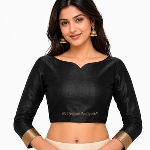 May include: Black long-sleeve blouse with a scoop neckline and gold trim on the cuffs. The blouse has a subtle sheen and a fitted silhouette. The text "@PriyankasBoutiqueIN" is printed on the bottom of the blouse.