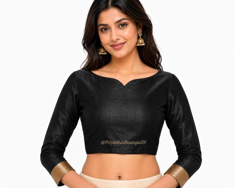 May include: Black long-sleeve blouse with a scoop neckline and gold trim on the cuffs. The blouse has a subtle sheen and a fitted silhouette. The text "@PriyankasBoutiqueIN" is printed on the bottom of the blouse.