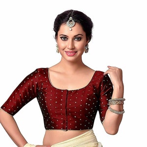 May include: A maroon, short-sleeved blouse with white polka dots and a hook and eye closure in the front. The blouse is made of a silky fabric and has a scoop neckline.