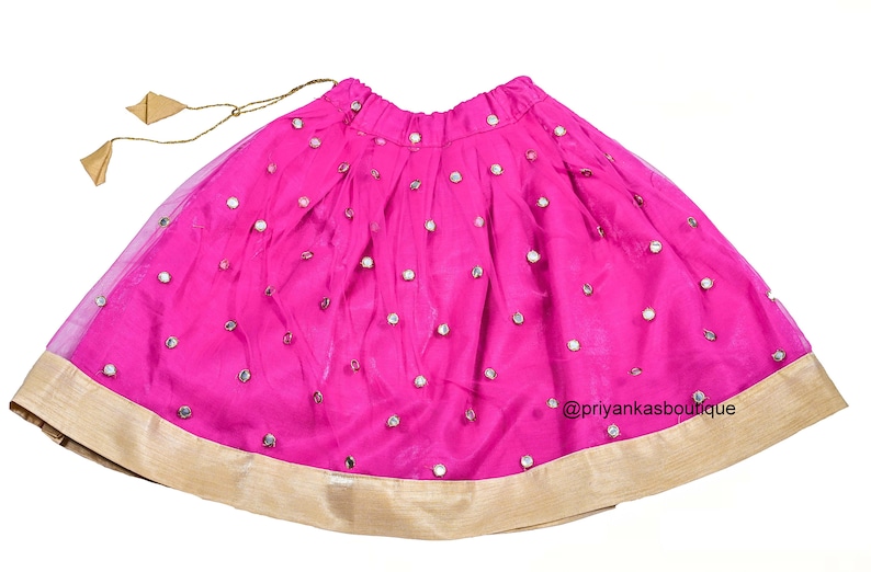 Op de afbeelding: Een roze rok met een gouden rand en spiegelversieringen. De rok heeft een trekkoord in de taille en is gemaakt van een transparante stof.