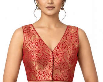 May include: A sleeveless red blouse featuring a metallic gold paisley pattern, a deep V-neckline, and a front button closure. The garment is crafted with a structured fit and a vibrant, intricate brocade-style design throughout the fabric.