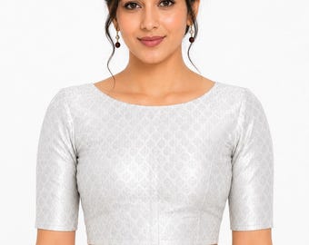 May include: A silver-colored, short-sleeved blouse with a subtle, repeating pattern. The blouse has a boat neckline and is cropped at the waist. The fabric appears to have a slight sheen. The model is wearing earrings.